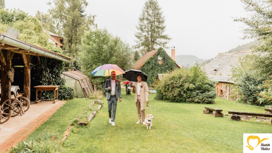 Ženiši s deštníky a pejskem jdou zahradou ke stodole na statku Vletice